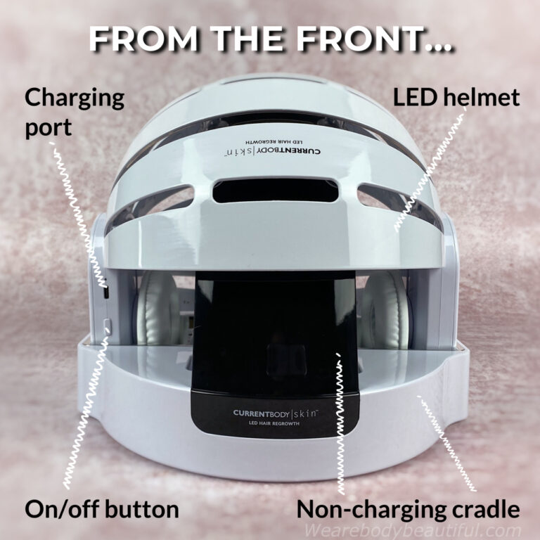 A view of the CurrentBody Skin LED hair regrowth from the front in the non-charging cradle. The charging port for the charging cable is on the helmet on the front of the right hand side outer earphone.