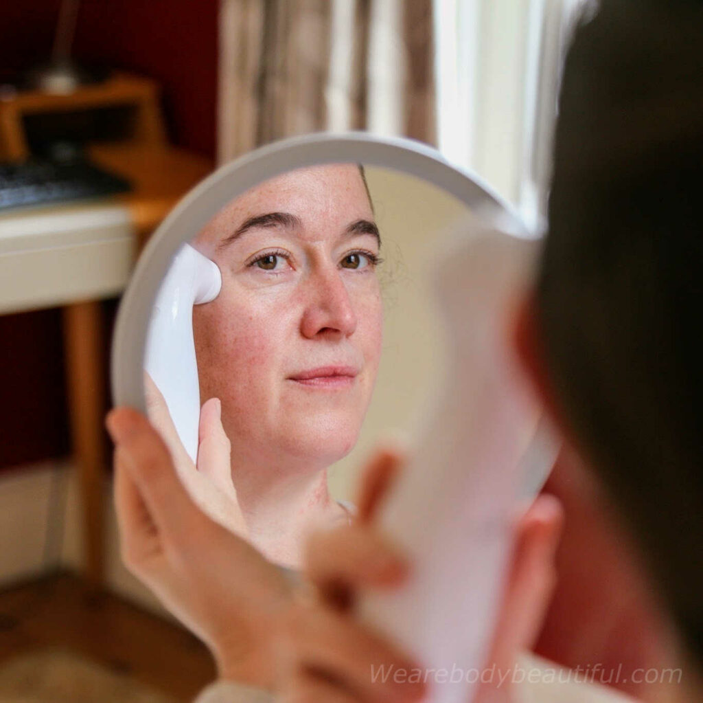 This is a photo of me testing the NIRA Pro skincare laser around my eyes reflected in a small, round handheld mirror.